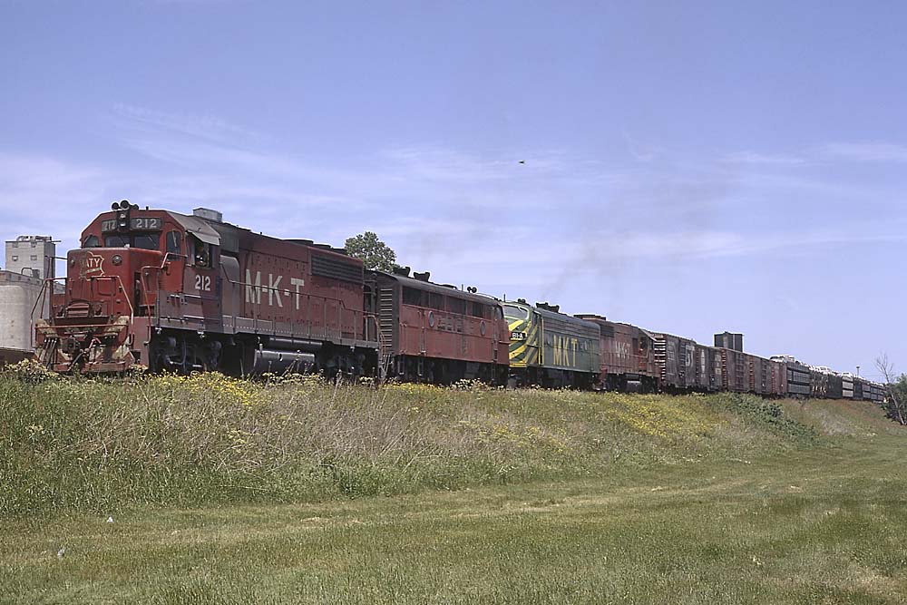 Mix of red-and-white and green-and-yellow Missouri-Kansas-Texas Railroad diesel locomotives on a freight train