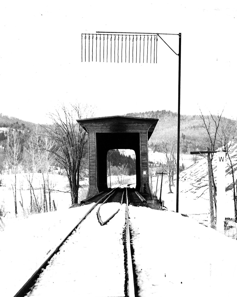 A row of ropes hang from a crossbar on a telltale in front of a covered railroad bridge in a snowy landscape in Vermont