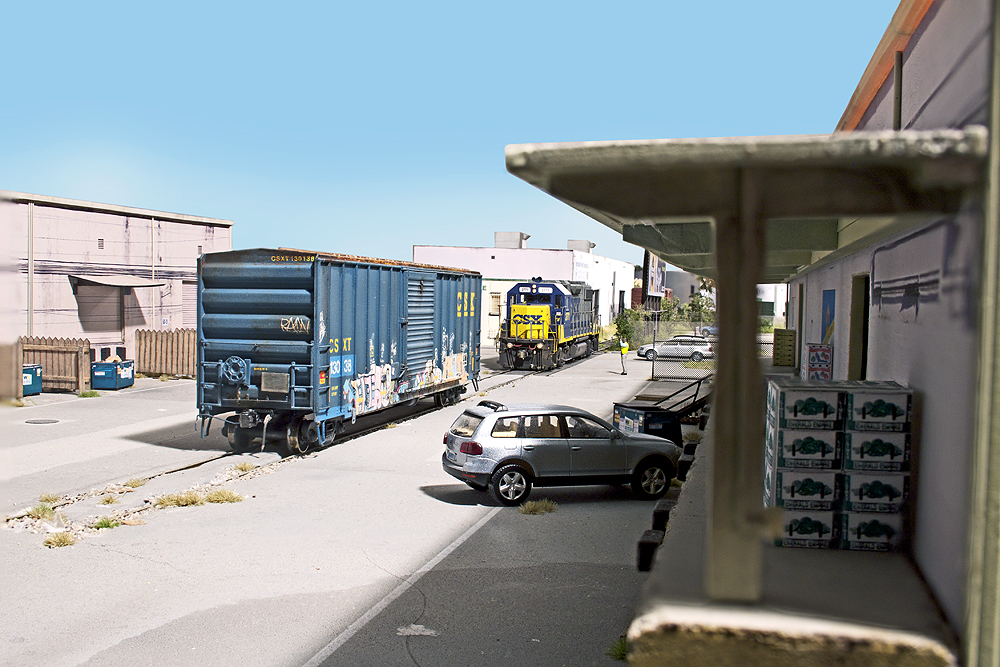 A blue boxcar with graffiti on it sits outside a warehouse