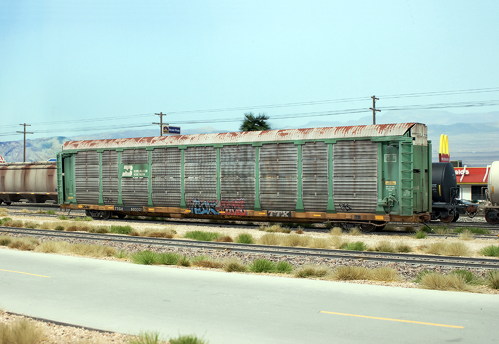 A well-weathered enclosed auto rack has graffiti on two panels near the center of the car