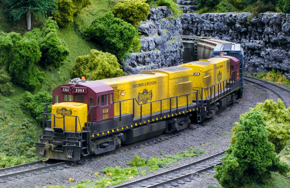 Yellow-and-maroon diesels pull a freight train through a rock cut on a model railroad