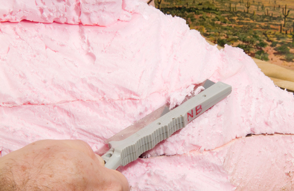 A razor saw is used to carve striations in a rock formation carved from pink foam insulation board