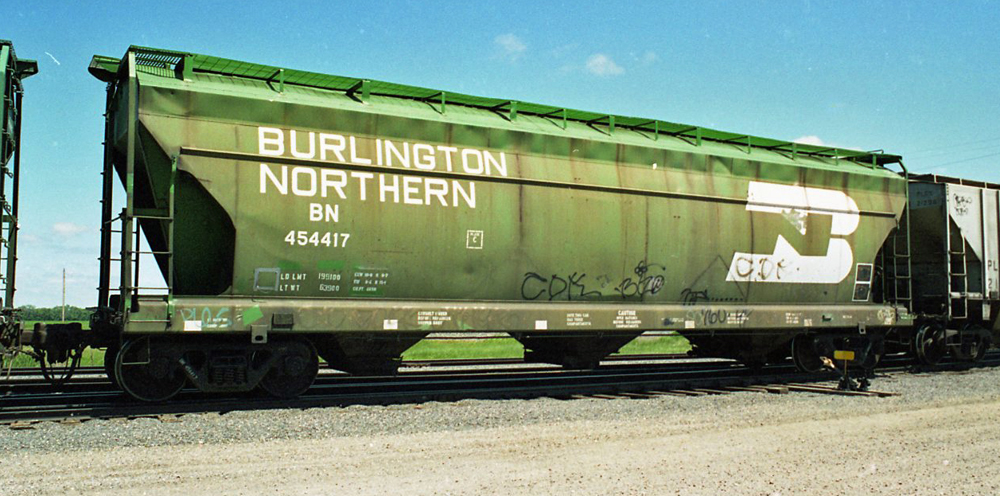 Photo of weathered green covered hopper in train on sunny day