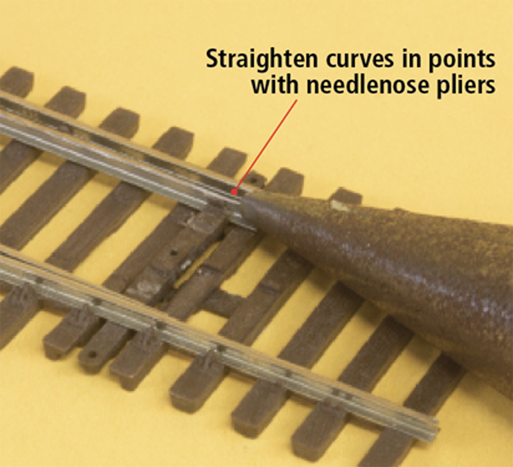 Pliers grasp and straighten a point in model railroad track.
