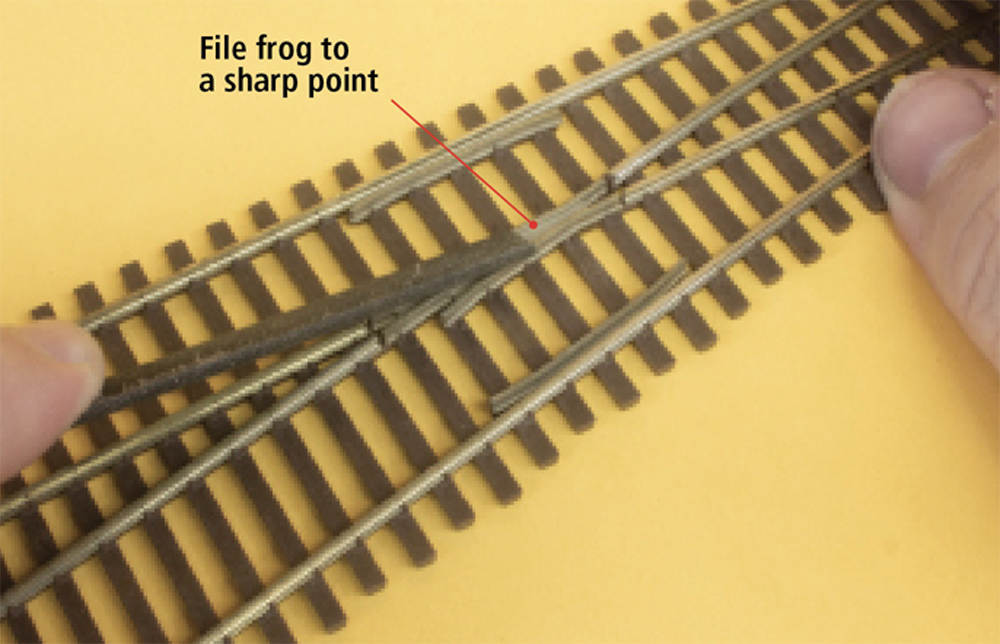 A dark grey file is used to file a section of brown track against a yellow background