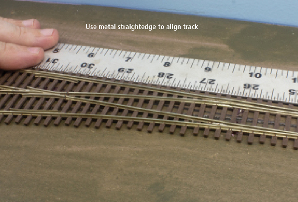 A white ruler lies next to a section of brown railroad track 