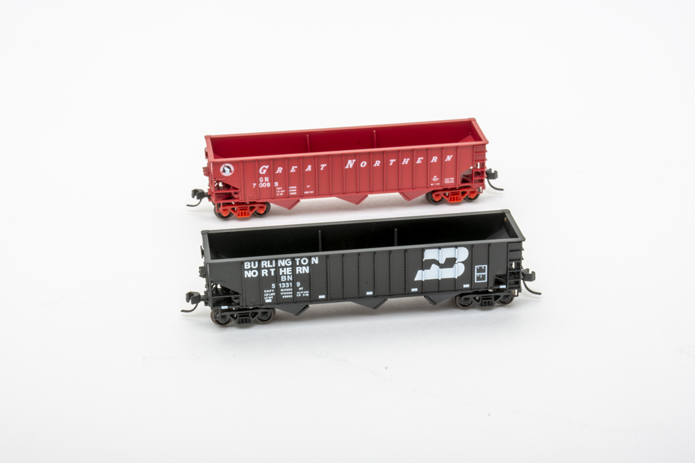 a black three-bay hopper car in the foreground and a red three-bay hopper car in the background