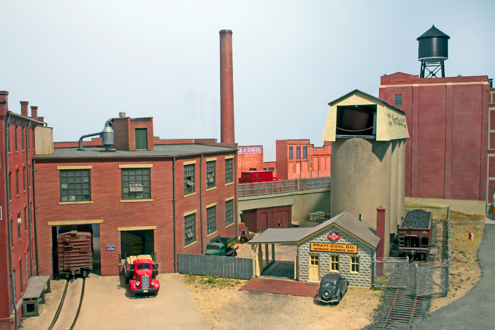 A model coal dealer located along a set of model railroad trcks, with a red truck near an opened loading bay door