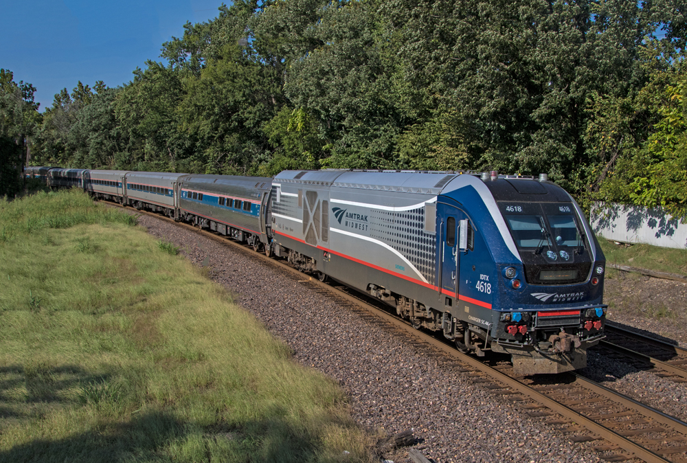 blue and grey passenger train passing a grove of trees