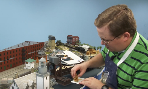 Man bent over model railroad layout working on fake water.
