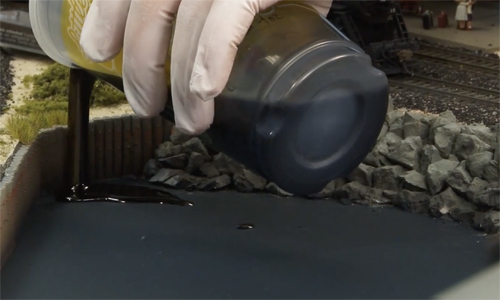 Hand pouring goo onto a model railroad harbor.