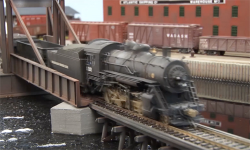 Model train locomotive operating over a bridge.