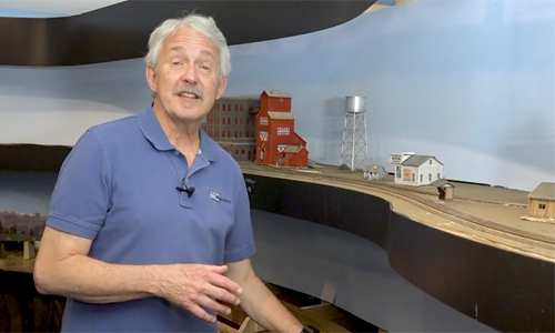 Man in front of a model train layout, gesturing.