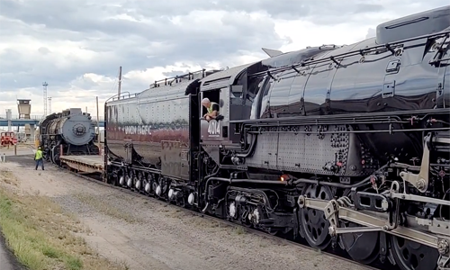 Giant steam locomotive pushing another one in a rail yard.