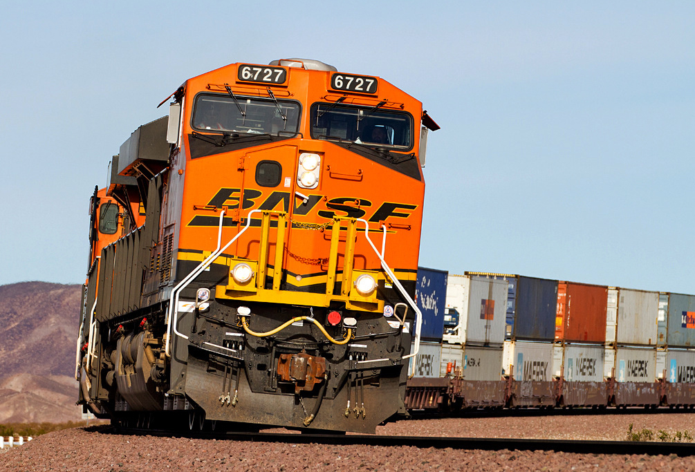 Orange locomotive with intermodal train on curve in desert