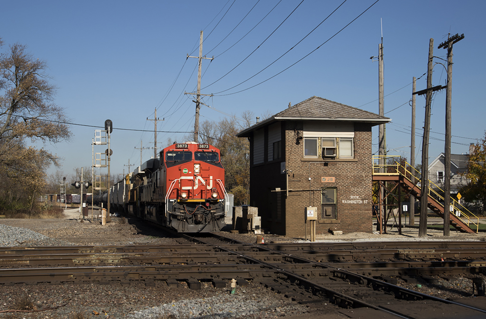 Locomotive with red front passes brick tower and prepares to cross two-track diamond