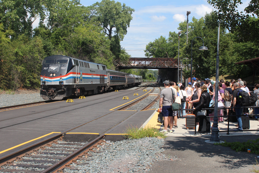 Train arrives at station where a large number of people wait on platform