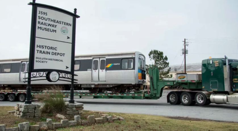 Rapid transit car on truck trailer passes sign for museum