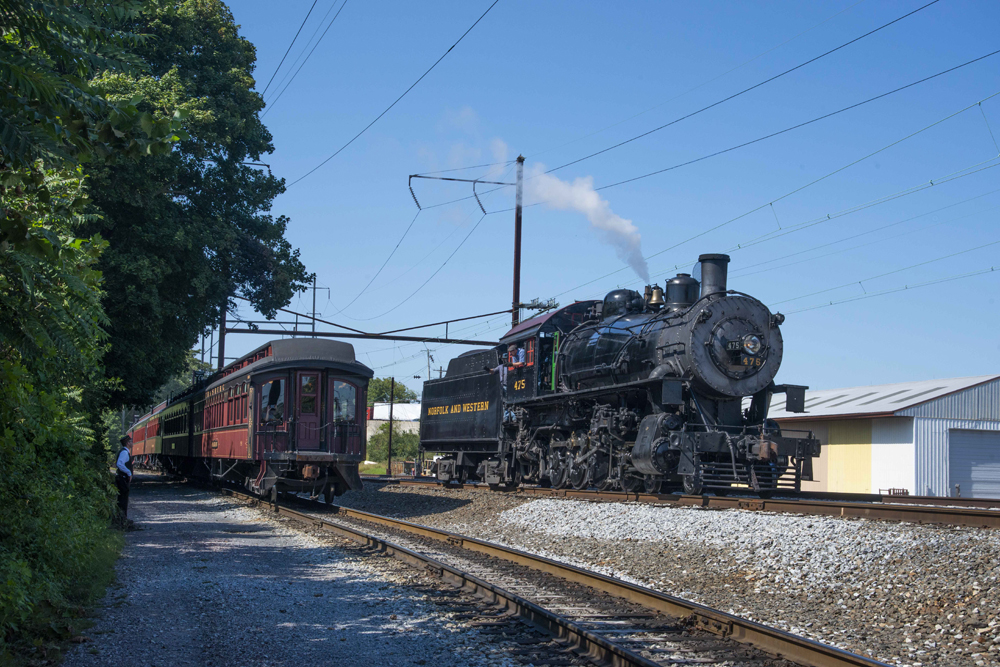 Steam locomotive passes standing passenger cars