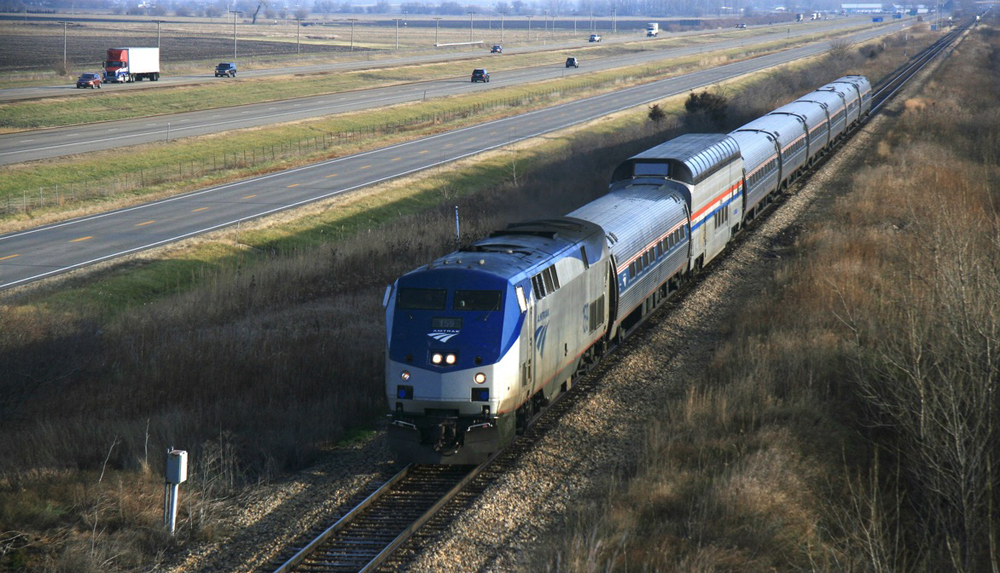 Passenger train with dome car operating next to highway