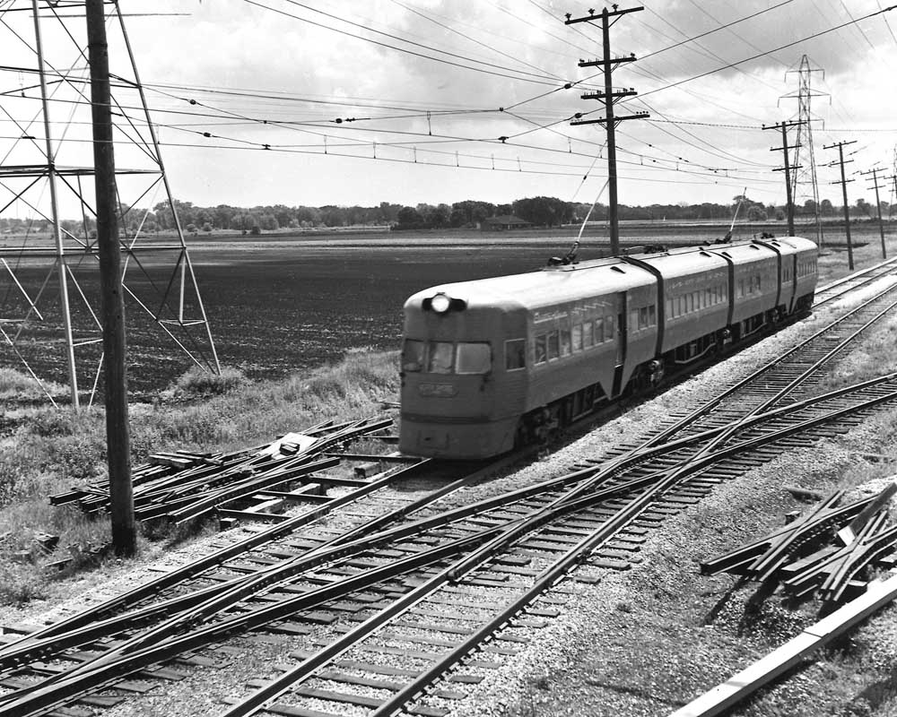 Streamlined electric passenger train crossing railroad tracks at grade during Chicago North Shore & Milwaukee history