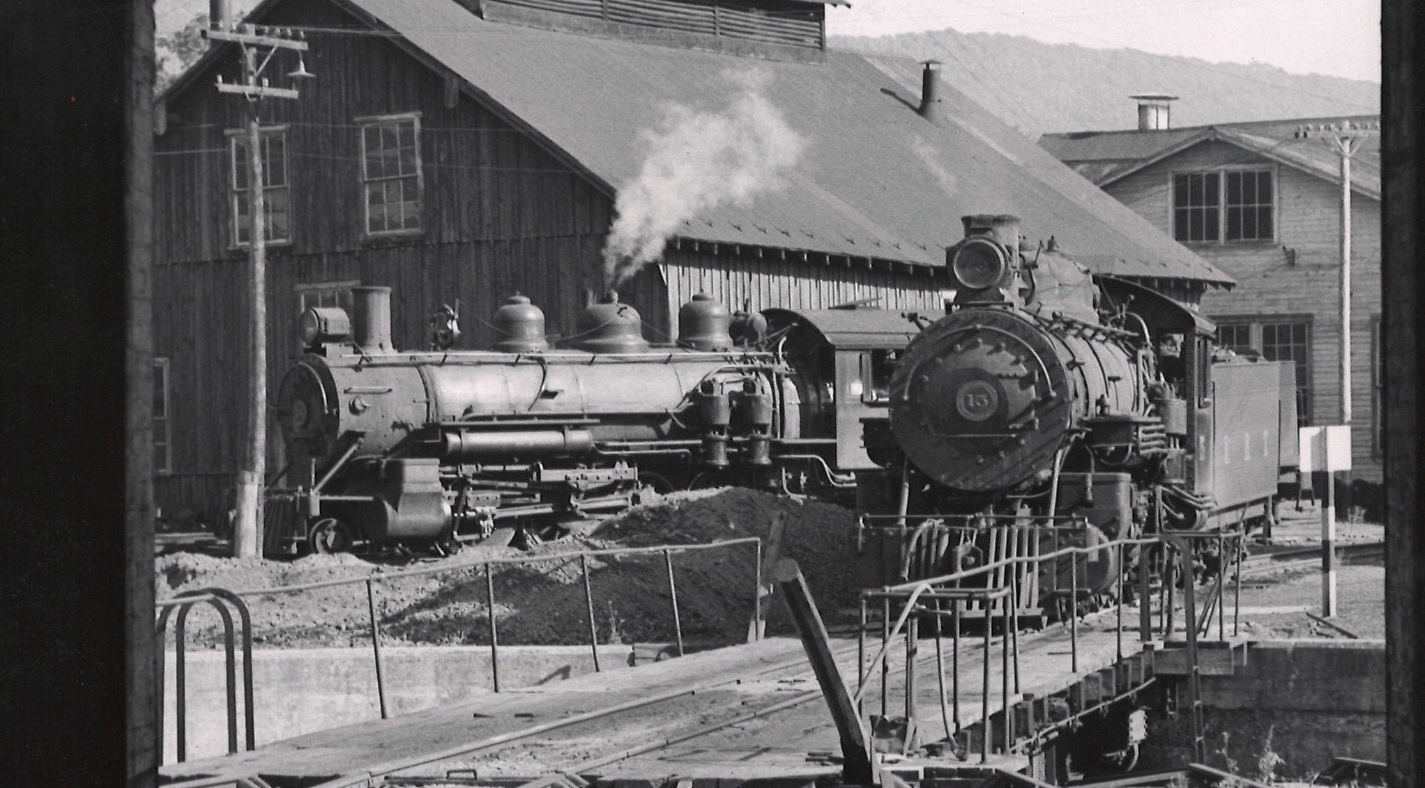 Two steam locomotives from outside the roundhouse door.