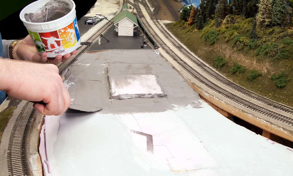 Gray plaster is troweled onto a terrain surface of pink foam board