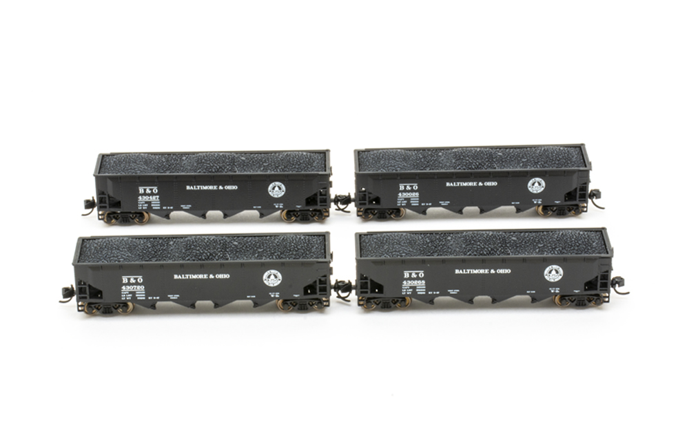 Four black freight hopper cars with load against a white background