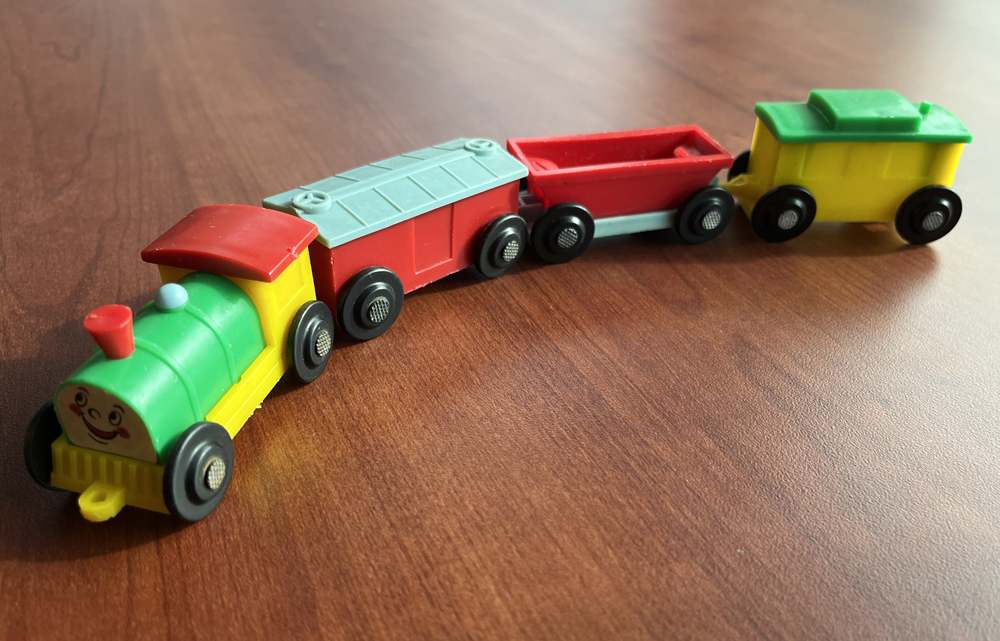 Toy train molded in green, red, yellow, and black plastic on a mahogany tabletop.