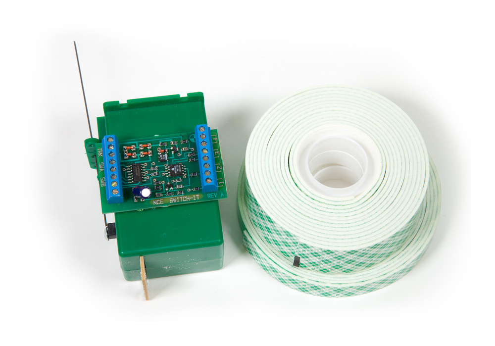 Handy tools for DCC wiring projects: A green decoder and a roll of electrical tape against a white background.