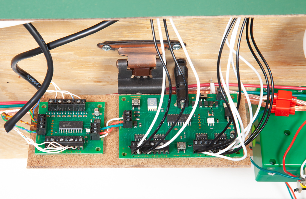 Green circuit boards are shown on the underside of a brown wooden table.