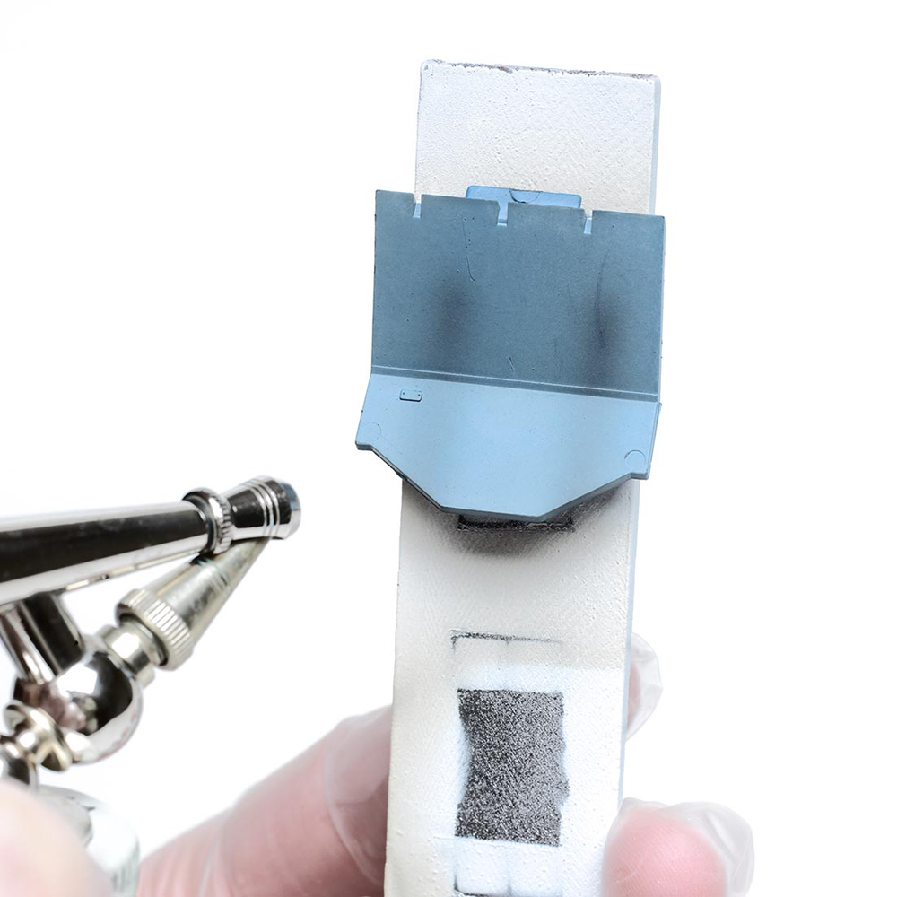 Weather with an airbrush: A airbrush is used along the backside of a blue model boxcar.