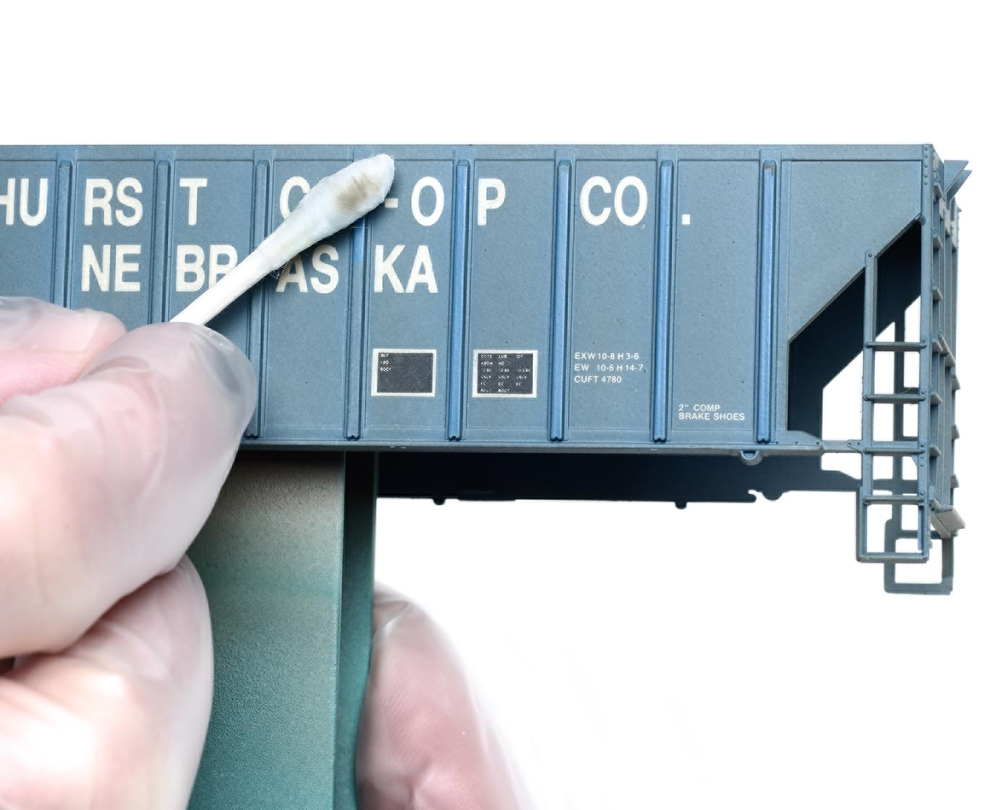 Weather with an airbrush: A cotton swab is used along the side of a blue model boxcar against a white background.