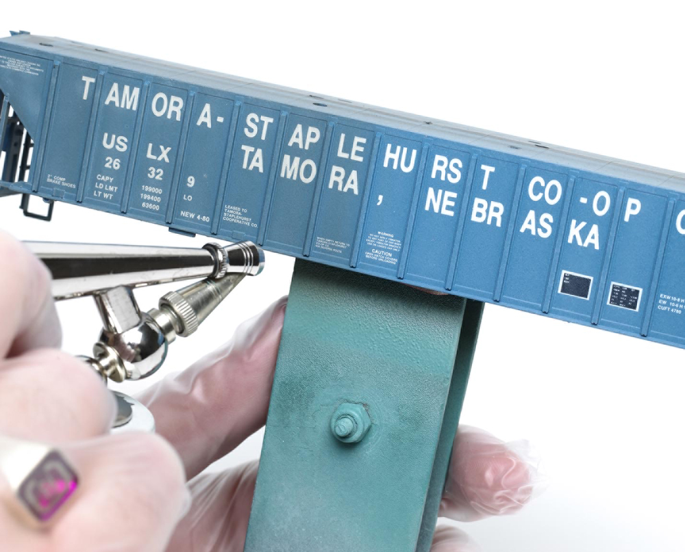 An image of an airbrush being used on a blue model boxcar