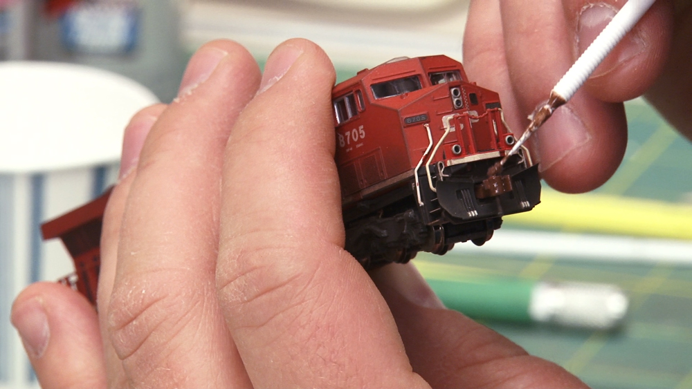 A red model locomotive is shown in someone's hand as details are pplied to the nose of the locomotive.