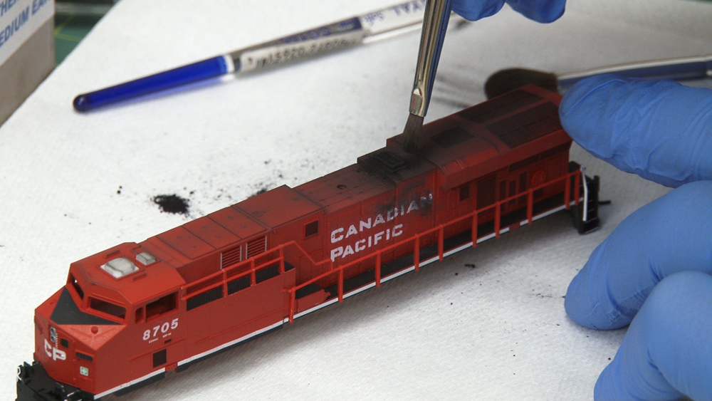 Weathering N scale locomotives: A red model locomotive sits on a white table as details are applied to the top of the model.