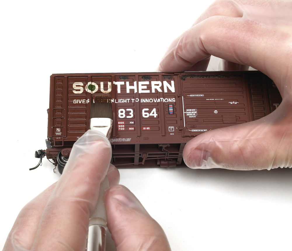 Weathering with artist's oils : a brush is shown in hand being used against the side of a brown boxcar