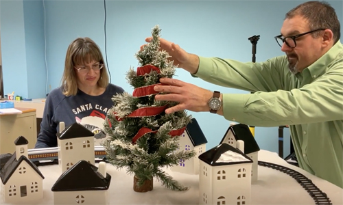 Woman and man setting up a Christmas toy train layout.