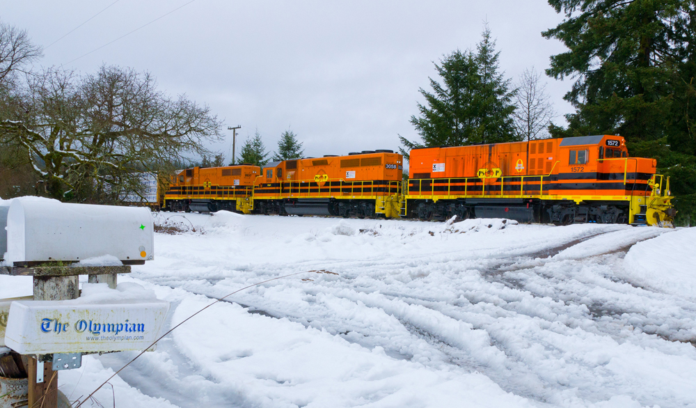 Orange locomotives power a train through a snowy scene.