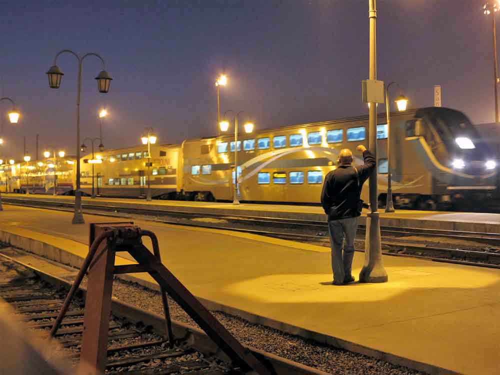 man leaning on pole looking at train