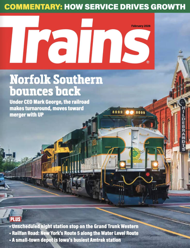 The February 2026 cover of Trains magazine which features a green and white locomotive moving through a small town