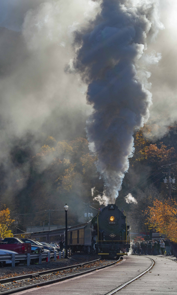 Steam locomotive under large plume of smoke as it rounds curve