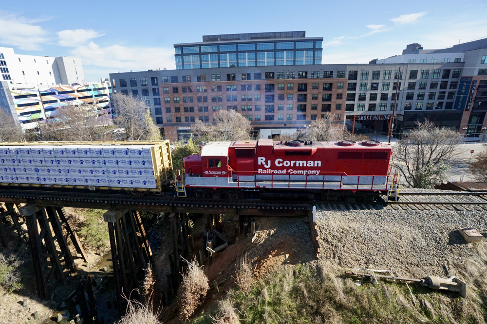 Red and white locomotive brings freight cars over bridge