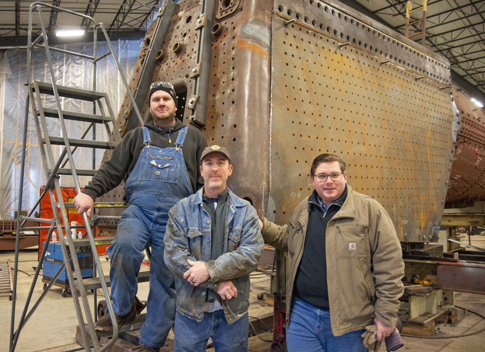 Three men standing in front of steam locomotive under construction