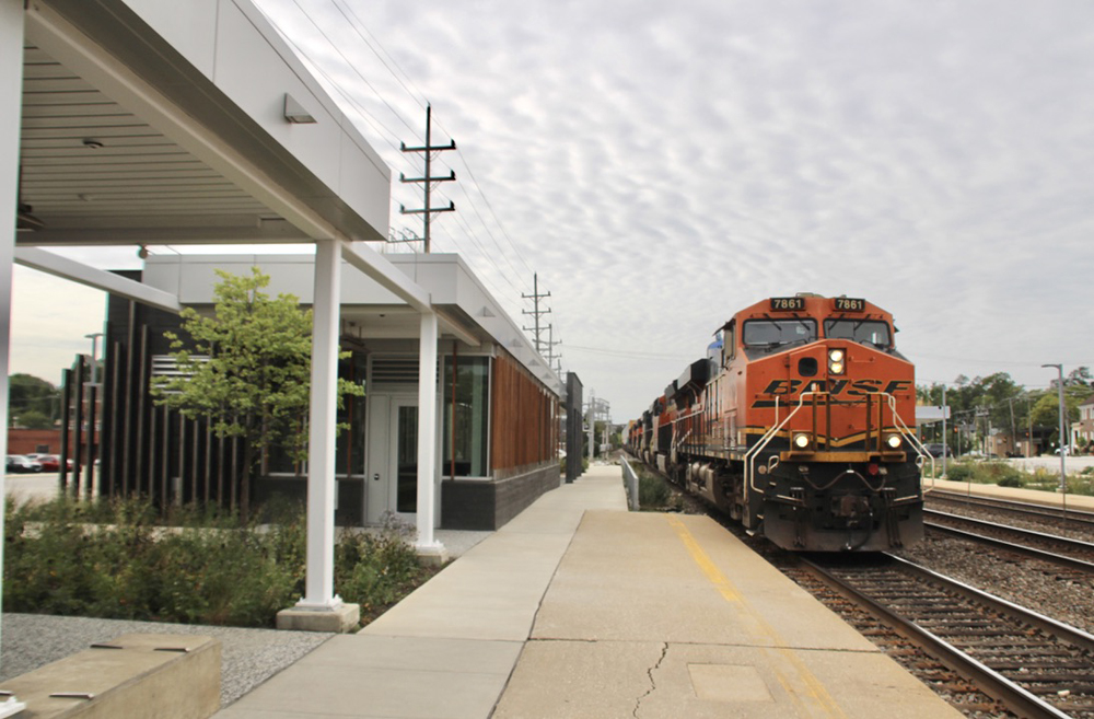 Freight train passes commuter station under cloudy skies