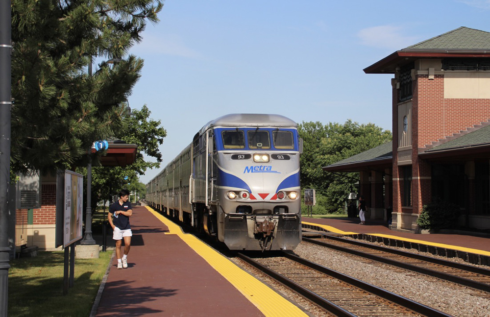 Commuter train with blue and silver locomotive arrives at brick station with central tower