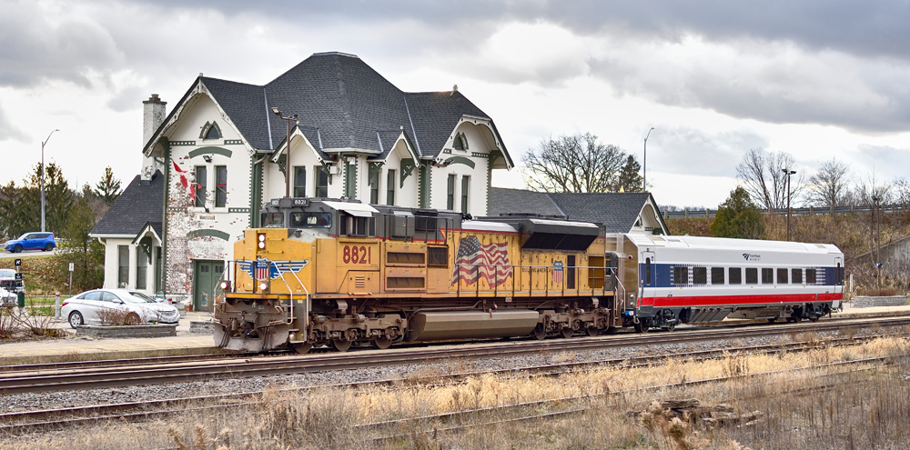 Freight locomotive and passenger car pass ornate white two-story passenger station