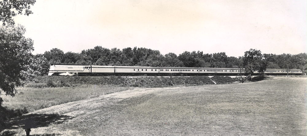 Streamlined steam train pauses in front of a field. 