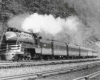 Streamlined steam locomotive with passenger train along hillside
