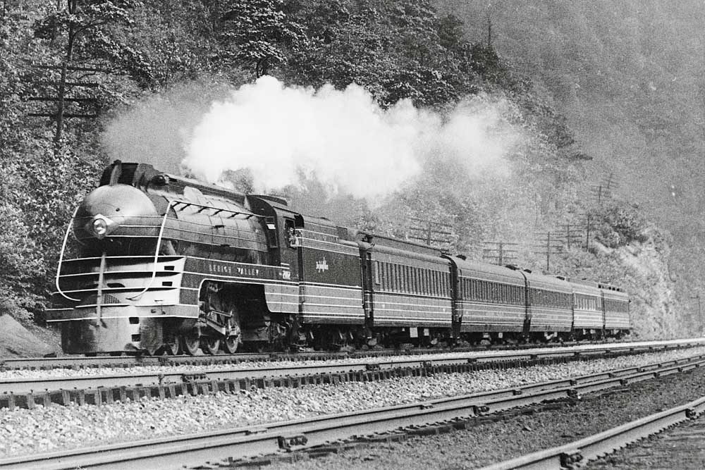 Streamlined steam locomotive with passenger train along hillside